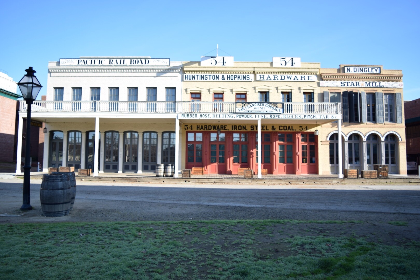 Historic buildings in Old Sacramento, including the Huntington & Hopkins Hardware store and other 19th-century storefronts with wooden barrels and a lamp post in front.